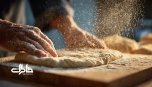 دست‌های نانوا در حال کشیدن خمیر بربری روی تخته و آماده‌سازی برای تنور. نان تازه داغ