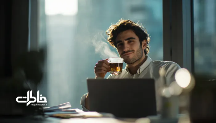 جوانی در روز کاری شلوغ پشت میز کار در حال نوشیدن چای با لبخند آرام و حس تمرکز. چای و کار