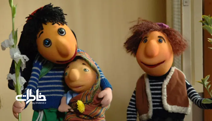 پرتره سینمایی از عروسک الهامگرفته از کلاهقرمزی با کلاه قرمز، پیراهن آبیوسفید راهراه، شلوار سبز و نگاه کودکانه در دکور تلویزیونی ایرانی