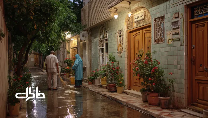 کوچهٔ تمیز ایرانی در غروب با دو همسایه که آرام جلوی خانه را آب‌وجارو می‌کنند در نور خنک و آرام. همسایه‌داری