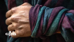 نمای نزدیک از دست مردی با دستمال یزدی نازک و لطیف به رنگ‌های زرشکی و سرمه‌ای که دور مچ پیچیده شده