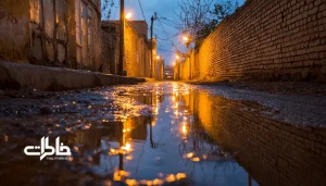 «انعکاس نور چراغ‌های محله روی زمین خیس کوچه ایرانی پس از باران». مجله خاطرات