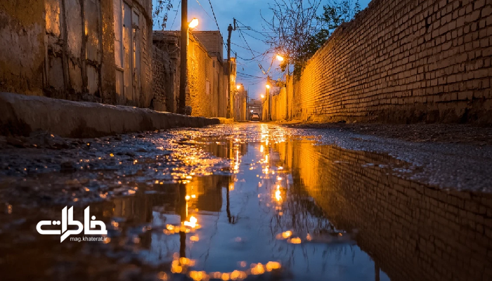 «انعکاس نور چراغ‌های محله روی زمین خیس کوچه ایرانی پس از باران». مجله خاطرات