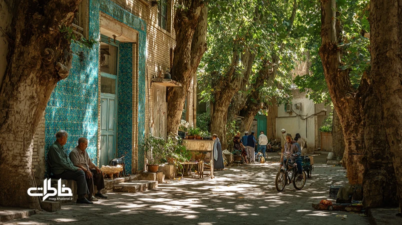 چنارهای کهن محله با سایه‌سار تابستان، نیمکت ساده و چای عصرانه در کنار انعکاس آب حوض؛ بازتاب صمیمیت محله و مفهوم چراغ محله