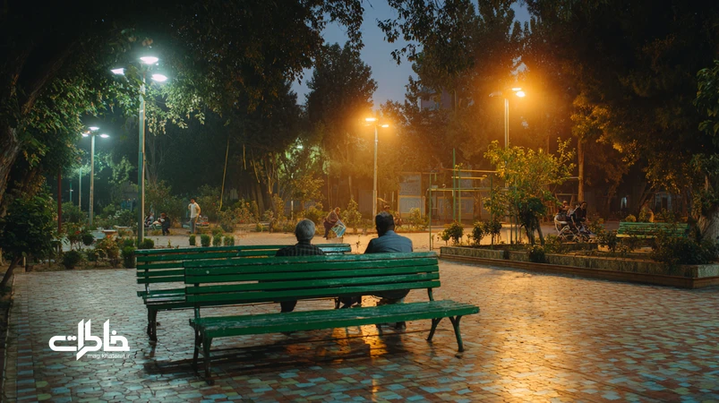 پارک محلهای ایرانی با نیمکتهای سبز زیر چراغهای زرد، نوجوانان در حال زمزمه، بازی توپ کودکان، کالسکهٔ بچه و حضور دوربین مداربسته و موبایلها.مجله خاطرات