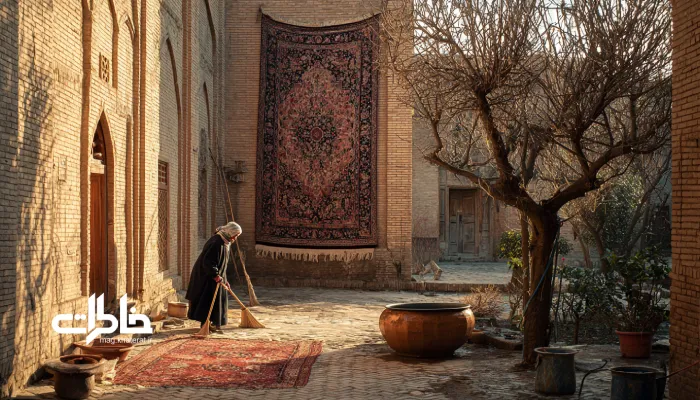 قالی‌کوبی در حیاط قدیمی؛ فرش ایرانی روی طناب، نور طلایی صبح و گرد و غبار معلق در هوا.