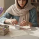 تصویر یک زن ایرانی در حال بسته‌بندی هدیه روی میز آشپزخانه با سنبل و یادداشت دست‌نویس؛ فضایی گرم و نوستالژیک درباره اسم هدیه