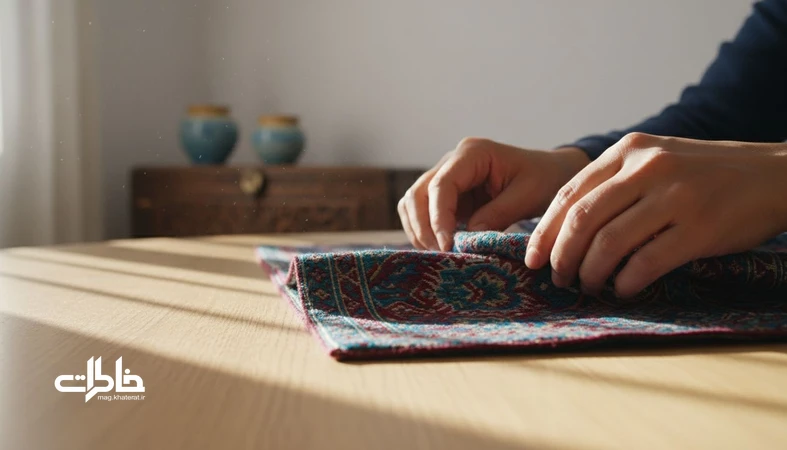 نمای نزدیک از تا زدن ترمه با دست های ایرانی و چین پارچه زیر نور صبح، نمادی از زمان تاخورده و خاطره در خانه ایرانی