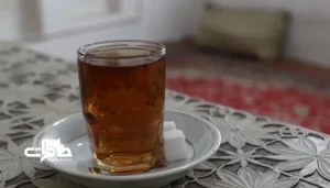 تصویر یک استکان چای و نلبعکی روی یک پارچه توری سفید قدیمی