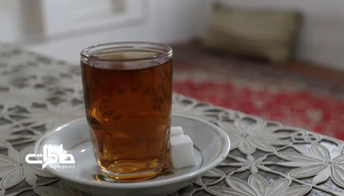 تصویر یک استکان چای و نلبعکی روی یک پارچه توری سفید قدیمی